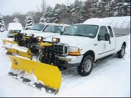 Image shows a fleet of white trucks with yellow snow plows..